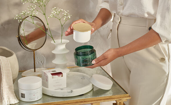 Een persoon die een potje The Ritual of Jing body cream navult, en een The Ritual of Sakura body cream refill op een kaptafel.